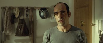 Movie still from “Sleep Tight” (2011), directed by Jaume Balagueró – A man in a gray shirt is looking at the camera; Close Up shot, Over the shoulder angle