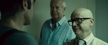 Movie still from “Sleep Tight” (2011), directed by Jaume Balagueró – A group of men standing next to each other in a room; Close Up shot, Over the shoulder angle