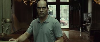 Movie still from “Sleep Tight” (2011), directed by Jaume Balagueró – A man with a bald head standing in front of a window; Close Up shot, Over the shoulder angle
