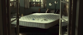 Movie still from “Sleep Tight” (2011), directed by Jaume Balagueró – An unmade bed in the middle of a room; Wide shot, High angle