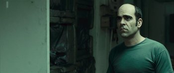 Movie still from “Sleep Tight” (2011), directed by Jaume Balagueró – A man with a bald head standing next to a wall; Close Up shot, Over the shoulder angle