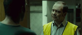 Movie still from “Sleep Tight” (2011), directed by Jaume Balagueró – An older man wearing a yellow and white jacket; Close Up shot, Over the shoulder angle