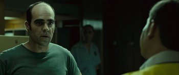 Movie still from “Sleep Tight” (2011), directed by Jaume Balagueró – A man standing next to another man in a room; Close Up shot, Over the shoulder angle
