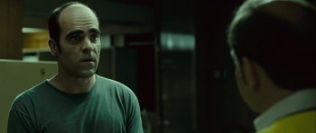 Movie still from “Sleep Tight” (2011), directed by Jaume Balagueró – A man with glasses is standing in a dark room; Close Up shot, Over the shoulder angle