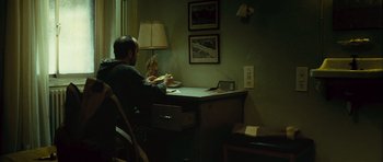 Movie still from “Sleep Tight” (2011), directed by Jaume Balagueró – A man sitting at a desk in front of a lamp; Medium shot, High angle