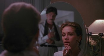 Movie still from “Sleeping with the Enemy” (1991), directed by Joseph Ruben – A woman putting lipstick on in front of a man in the mirror; Close Up shot, Over the shoulder angle