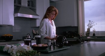 Movie still from “Sleeping with the Enemy” (1991), directed by Joseph Ruben – A woman in a white shirt is in a kitchen; Medium shot, Low angle