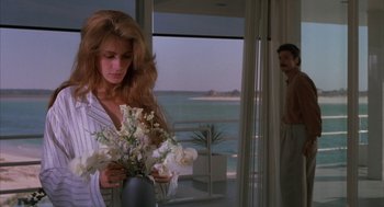Movie still from “Sleeping with the Enemy” (1991), directed by Joseph Ruben – A woman holding a vase of flowers in front of the ocean; Medium shot, Over the shoulder angle