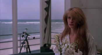 Movie still from “Sleeping with the Enemy” (1991), directed by Joseph Ruben – A woman standing in front of the ocean holding a vase of flowers; Medium shot, Over the shoulder angle