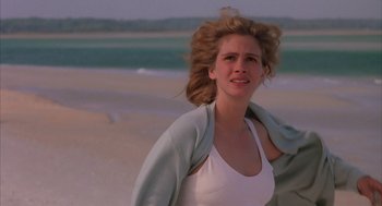 Movie still from “Sleeping with the Enemy” (1991), directed by Joseph Ruben – A beautiful woman standing on the beach in a white tank top; Close Up shot, Over the shoulder angle