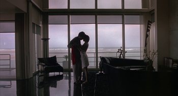 Movie still from “Sleeping with the Enemy” (1991), directed by Joseph Ruben – A man and a woman kissing in front of a large window; Wide shot, Low angle