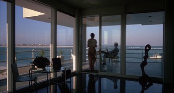 Movie still from “Sleeping with the Enemy” (1991), directed by Joseph Ruben – A woman standing in front of a window looking out at the ocean; Wide shot, High angle