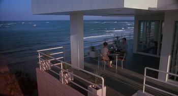 Movie still from “Sleeping with the Enemy” (1991), directed by Joseph Ruben – Two people sitting at a table on a balcony overlooking the ocean; Extreme Wide shot, High angle