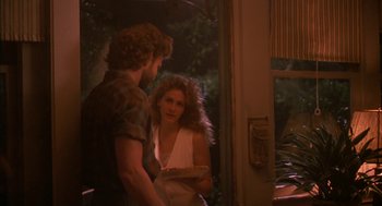 Movie still from “Sleeping with the Enemy” (1991), directed by Joseph Ruben – A man and a woman standing next to each other holding a cake; Medium shot, Over the shoulder angle