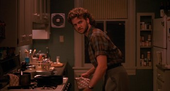 Movie still from “Sleeping with the Enemy” (1991), directed by Joseph Ruben – A man standing in front of an oven in a kitchen; Medium shot, Over the shoulder angle