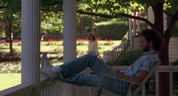 Movie still from “Sleeping with the Enemy” (1991), directed by Joseph Ruben – A person on a porch swing with a woman in the background; Wide shot, Low angle
