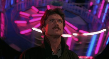 Movie still from “Sleeping with the Enemy” (1991), directed by Joseph Ruben – A man with a mustache standing in front of a ferris wheel at night; Close Up shot, Low angle