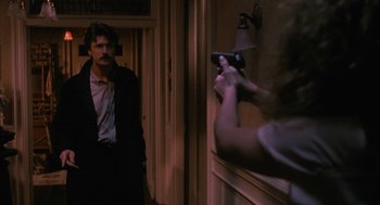 Movie still from “Sleeping with the Enemy” (1991), directed by Joseph Ruben – A man in a suit and tie holding a game controller in front of a mirror; Medium shot, Over the shoulder angle