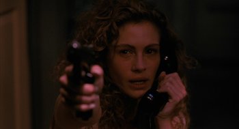Movie still from “Sleeping with the Enemy” (1991), directed by Joseph Ruben – A woman holding a gun and a cell phone in her hand; Close Up shot, Low angle