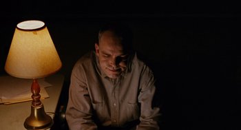 Movie still from “Sling Blade” (1996), directed by Billy Bob Thornton – A man sitting in a dark room with a lamp in front of him; Medium shot, Low angle