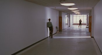 Movie still from “Sling Blade” (1996), directed by Billy Bob Thornton – A man leaning against a wall in an office building; Wide shot, Over the shoulder angle