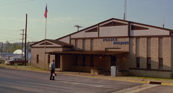 Movie still from “Sling Blade” (1996), directed by Billy Bob Thornton – A man walking down the street in front of a police building; Extreme Wide shot, Low angle