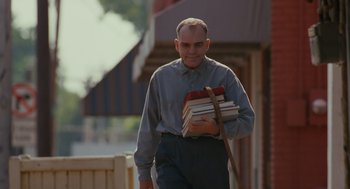 Movie still from “Sling Blade” (1996), directed by Billy Bob Thornton – A man is walking with a stack of books; Medium shot, Low angle