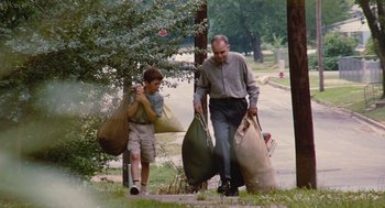 Movie still from “Sling Blade” (1996), directed by Billy Bob Thornton – A man and a boy walking down a sidewalk with bags; Wide shot, Low angle