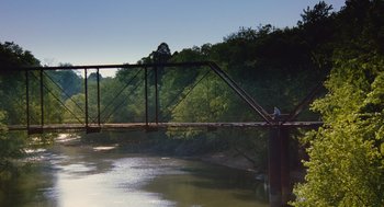 Movie still from “Sling Blade” (1996), directed by Billy Bob Thornton – A person standing on a bridge over a river; Extreme Wide shot, High angle