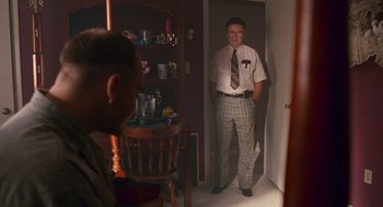Movie still from “Sling Blade” (1996), directed by Billy Bob Thornton – A man in a tie standing next to a chair in a room; Medium shot, Over the shoulder angle