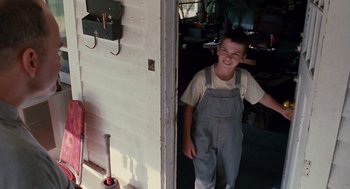 Movie still from “Sling Blade” (1996), directed by Billy Bob Thornton – A young boy in overalls standing in front of an open door; Medium shot, Low angle