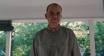 Movie still from “Sling Blade” (1996), directed by Billy Bob Thornton – A man wearing a gray shirt standing in front of trees; Medium shot, Low angle