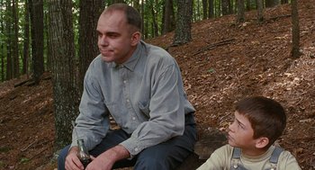 Movie still from “Sling Blade” (1996), directed by Billy Bob Thornton – A man sitting on the ground next to another man; Medium shot, Low angle