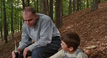 Movie still from “Sling Blade” (1996), directed by Billy Bob Thornton – A man and a boy sitting on the ground in the woods; Medium shot, Over the shoulder angle