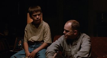 Movie still from “Sling Blade” (1996), directed by Billy Bob Thornton – A man sitting next to a boy in a room; Medium shot, Over the shoulder angle