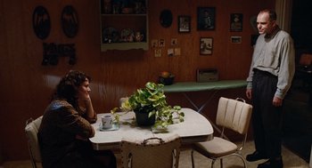 Movie still from “Sling Blade” (1996), directed by Billy Bob Thornton – A woman sitting at a table with a plant on top of it; Wide shot, High angle