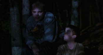 Movie still from “Sling Blade” (1996), directed by Billy Bob Thornton – A man and a boy sitting next to each other in the dark; Medium shot, Over the shoulder angle