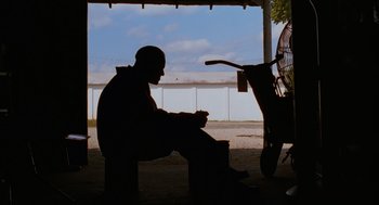 Movie still from “Sling Blade” (1996), directed by Billy Bob Thornton – A man sitting on a bench in front of a fan; Wide shot, Low angle