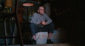Movie still from “Sling Blade” (1996), directed by Billy Bob Thornton – A man sitting on top of a box in a dark room; Medium shot, Low angle