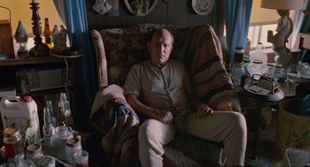 Movie still from “Sling Blade” (1996), directed by Billy Bob Thornton – An older man sitting on a couch in a living room; Medium shot, High angle
