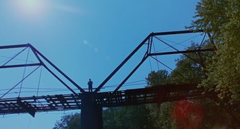 Movie still from “Sling Blade” (1996), directed by Billy Bob Thornton – A man standing on a bridge looking up at the sky; Extreme Wide shot, Low angle
