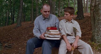 Movie still from “Sling Blade” (1996), directed by Billy Bob Thornton – A man sitting next to a boy holding a stack of books; Medium shot, Low angle