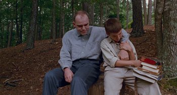 Movie still from “Sling Blade” (1996), directed by Billy Bob Thornton – A man sitting next to a young boy on a bench; Medium shot, Low angle