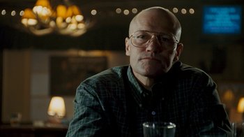 Movie still from “Slither” (2006), directed by James Gunn – A bald man with glasses is sitting at a table with a drink; Close Up shot, Low angle