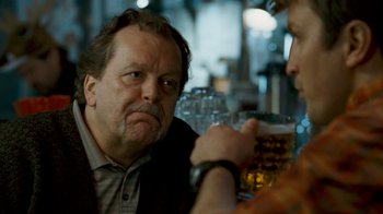 Movie still from “Slither” (2006), directed by James Gunn – A man sitting at a table with a glass of beer in front of him; Close Up shot, Over the shoulder angle