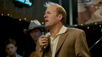Movie still from “Slither” (2006), directed by James Gunn – A man in a brown jacket is singing into a microphone; Close Up shot, Low angle