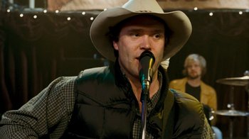 Movie still from “Slither” (2006), directed by James Gunn – A man wearing a cowboy hat is singing into a microphone; Close Up shot, Over the shoulder angle