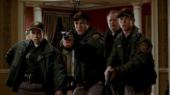 Movie still from “Slither” (2006), directed by James Gunn – A group of men standing next to each other holding guns; Medium shot, Low angle