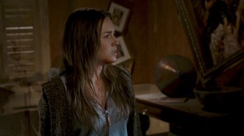 Movie still from “Slither” (2006), directed by James Gunn – A woman with long brown hair is standing in front of a table; Medium shot, Over the shoulder angle