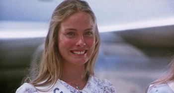 Movie still from “Smile” (1975), directed by Michael Ritchie – A woman smiles for a picture in front of an airplane; Close Up shot, Low angle
